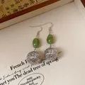 Macro view of vintage Chinese style earrings with green resin and silver filigree balls. - Hook Style / Silver