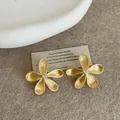Detailed close-up of golden flower stud earrings with textured petals on a beige background. - Five-Petal Brushed Style (Silver Post) / Gold