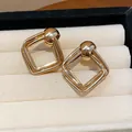 Primo piano di orecchini geometrici minimalisti a rombo dorati in una scatola portagioie. - Rombo / Oro
