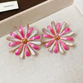 Macro detail of elegant pink and white flower drip oil stud earrings on a display tray. - Enamel Flower Style / Pink