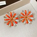Detail shot of orange and white enamel flower stud earrings on a textured beige tray - Enamel Flower Style / Orange