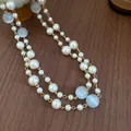 Detailansicht einer vintage mehrlagigen Kette mit Perlen und Katzenaugenstein auf Holz. - Doppellagiger Perlenstil / Gold-Weiß