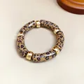 Vista detallada de una pulsera de acrílico con estampado de leopardo y piezas doradas - Café Claro