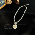 Detail view of an elegant pearl necklace featuring a gold-plated heart pendant with stones. - Camellia Heart Necklace / Gold