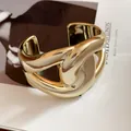 Chunky gold-toned horsebit cuff bracelet with a high-shine metallic finish and twisted knot design. - Cross Design / Gold