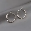 Macro detail of silver twisted hoop earrings with polished finish on grey fabric background - Twisted Style (1#) / Silver