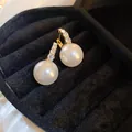 Close-up detail of elegant gold-toned earrings with crystals and large white pearls - White