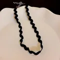 Close-up detail of a minimalist black wavy fabric choker necklace displayed on white ceramic - Unique Black Large Wave Ribbed Style