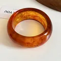 Macro detail of amber resin bangle with marble texture and warm translucent finish - Brown