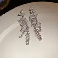 Detailed view of sparkling rhinestone butterfly tassel earrings on a white plate. - Silver-Transparent