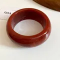 Close-up of a thick dark red resin bangle with marble texture on white surface - Brown