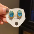 Close-up of vintage oval blue crystal earrings with ornate gold-tone settings. - Oval Granular Texture Style (15) / Gold with Blue