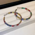 Makroaufnahme bunter rechteckiger Zirkonia-Creolen auf einer weichen weißen Samtschmuckschale - Geometrische Creole / Silber
