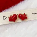 Macro detail of red enamel pony earrings with golden wings on cozy white faux fur - Red Pony Style / Red