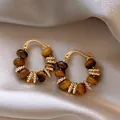 Close-up of gold-plated hoop earrings with natural tiger eye beads on silk fabric. - Hoop Style (1#) / Gold And Coffee