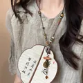 Gros plan d'un collier en perles de bois Zen avec pendentif éventail sur chemise en lin - Style Lune Marron (4#)