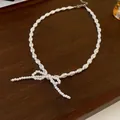Elegant white pearl necklace featuring a delicate bow-shaped pendant on dark wood background - Necklace Style 12