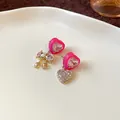 Macro detail of asymmetric pink heart earrings with rhinestone bow and heart charms. - Gold-Pink