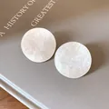 Close-up of minimalist round acrylic stud earrings with a elegant pearlescent marble texture - White