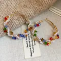 Detalle de pendientes de aro dorados con perlas y cristales de colores sobre fondo texturizado. - Pequeño / Multicolor