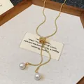 Close-up of elegant gold snake chain necklace with twin pearl pendants on a vintage card. - Gold
