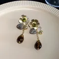 Macro view of vintage floral heart drop earrings with green rhinestones and brown beads - Flower Heart Dangle Style / Gold