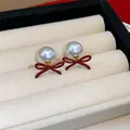 Close-up of vintage red bow and pearl stud earrings on a beige jewelry display tray - Red-White