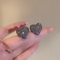 Primo piano dettagliato di orecchini a lobo a cuore con cristalli scintillanti sulle dita - Forma di Cuore / Grigio
