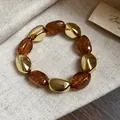 Dettaglio di un bracciale elastico retrò in acrilico ambra con perle dorate irregolari. - Bracciale / Caffè Scuro