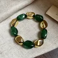 Dettaglio macro di un bracciale elastico vintage in acrilico con glitter verdi e perle oro - Bracciale / Verde