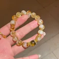 Primer plano detallado de una pulsera de citrino con dijes dorados y cuenta de ojo de tigre - Estilo Bola Flor Circonita Citrino Ojo de Tigre(6) / Embalaje Caja de Suspensión