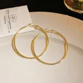 Macro view of large golden minimalist hoop earrings displayed on white ceramic plate - 5cm / Gold