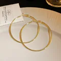 Close-up of oversized gold-tone minimalist hoop earrings on a white elegant plate - 6cm / Gold