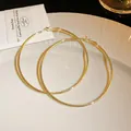 Close-up of minimalist thin gold metal hoop earrings displayed on a white textured plate - 7cm / Gold