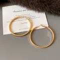 Macro view of gold-colored minimalist hoop earrings on a textured grey background - Medium (HE23305) / Diameter 45mm / Gold