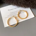 Detail view of stylish gold minimalist hoop earrings on decorative white card backdrop - Small (HE23305) / Diameter 29mm / Gold