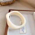 Primer plano de un brazalete de acrílico crema con diseño ondulado minimalista - Estilo Retorcido / Blanco