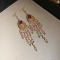 Nahaufnahme von Vintage-Quastenohrringen im Hofstil mit lila Tropfensteckern und Perlenfransen - Rosa