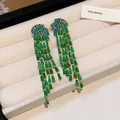Detailed macro view of elegant green and teal zircon tassel drop earrings on beige tray - Gold-Green