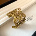 Detailopname van een vintage gouden manchetarmband met opengewerkt bloemenmotief - Armring (HB4380) / Goud