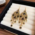 Close-up detail of vintage teardrop earrings with black rhinestones and golden tassels. - Hook Style / Gold