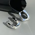 Macro view of polished silver geometric U-shaped hoop earrings on grey textured leather - Ear Buckle / Silver