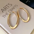 Detailed view of elegant gold-toned oval twisted hoop earrings resting on a book surface - Gold