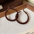 Primo piano di orecchini a cerchio floccati marroni con texture vellutata e design sobrio - Ago d'argento / Marrone