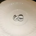 Close-up of matte brushed silver bean-shaped stud earrings on a white ceramic plate - Silver