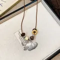 Detailed close-up shot of vintage ginkgo leaf pendant necklace with natural wooden beads - Necklace-Coffee-Silver