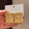 Elegant gold square earrings with a textured tree bark finish displayed on a white card holder - Gold