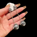 Detailed close-up view of silver metallic ball drop earrings held in hand for scale - Ball Tassel Style / Silver
