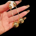 Close-up of golden sphere drop earrings with minimalist long bar design on a black background - Ball Tassel Style / Gold