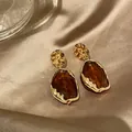 Dettaglio di orecchini vintage irregolari con resina ambra e finitura dorata - Marrone